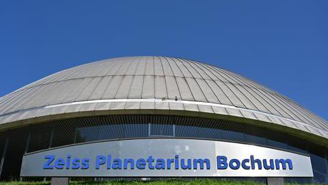 Außenaufnahme des Zeiss Planetarium Bochum. Vor dem Gebäude ist ein großes Schild auf dem „Zeiss Planetarium Bochum“ steht.