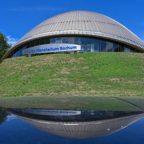 Das Bild zeigt die Kuppel des Planetariums von außen vor einer grünen Wiese.