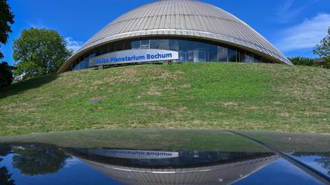 Das Bild zeigt die Kuppel des Planetariums von außen vor einer grünen Wiese.