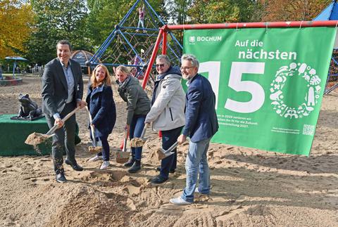 Fünf Personen stehen mit Schaufeln beim Spatenstich im Stadtpark vor einem grünen Banner.