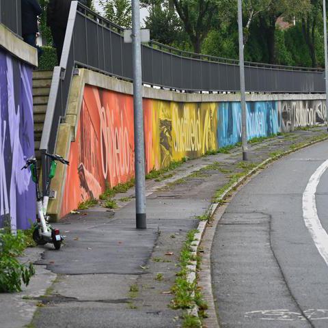 Eine Straße mit einer Kurve. Am Rand ist eine Mauer mit bunten Bildern.