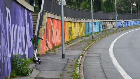 Eine Straße mit einer Kurve. Am Rand ist eine Mauer mit bunten Bildern.